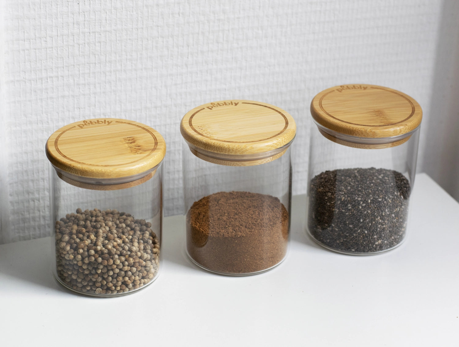 Set aus drei runden Vorratsgläsern von Pebbly mit Bambusdeckeln, ideal für die umweltfreundliche und dekorative Lagerung von Lebensmitteln.