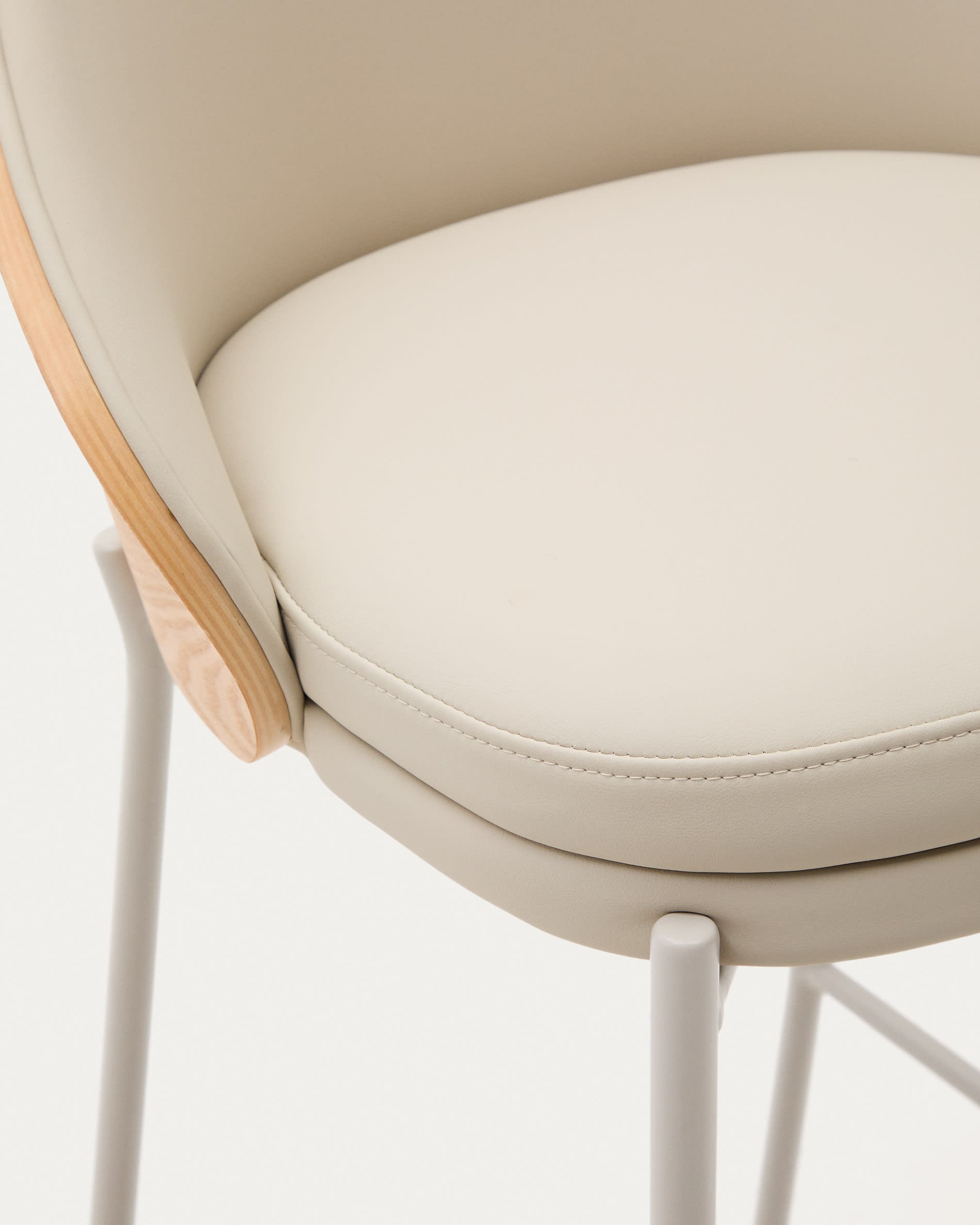 Eamy Hocker von Kave Home: Beigefarbenes Kunstleder, naturfarbenes Eschenfurnier und elegante Metallakzente – perfekt für moderne Wohnräume.