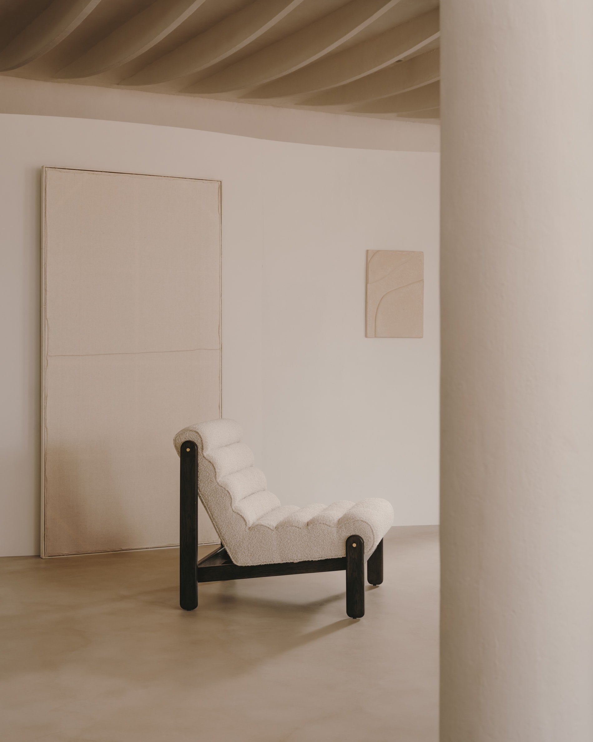 Der Sessel Magira vereint weisses Bouclé mit dunklem Eichenholz, bietet luxuriösen Komfort und ist ein stilvoller Blickfang.