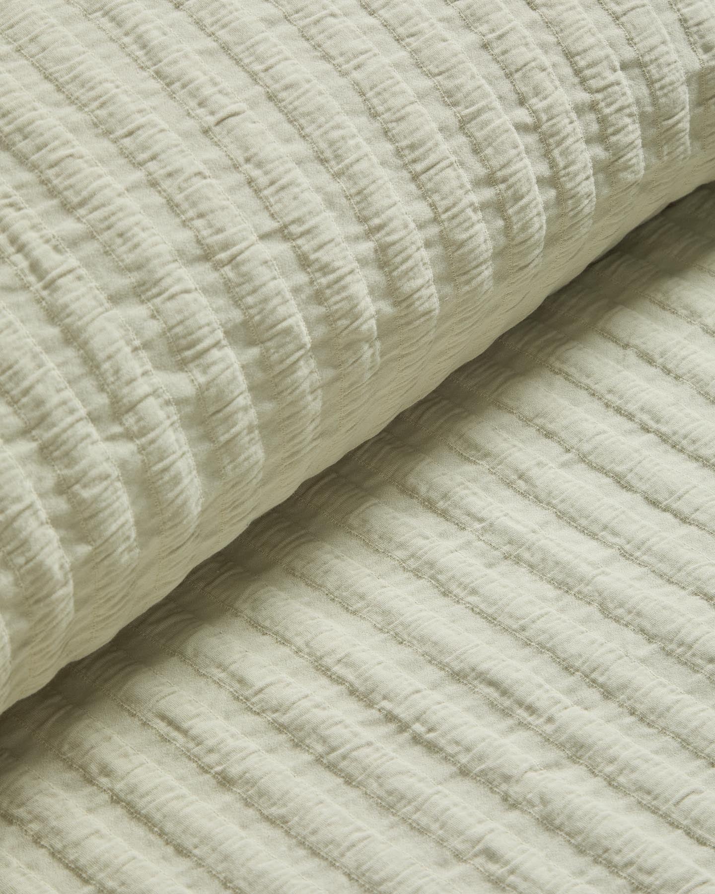 Zarte Tagesdecke Rilune in sanftem Hellgrün, gefertigt aus 100 % Baumwolle mit Reliefstreifen, perfekt für stilvolle Babybetten.